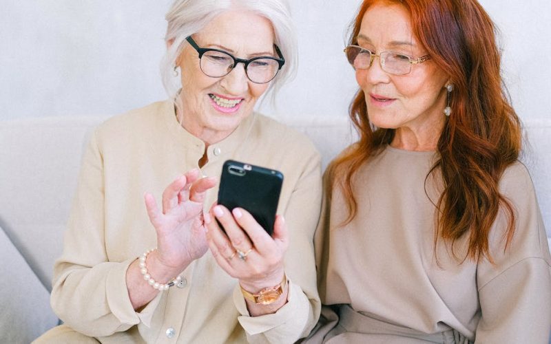 happy-elderly-elegant-trendy-women-looking-at-screen-of-mobile-phone-and-shopping-online-while-resti